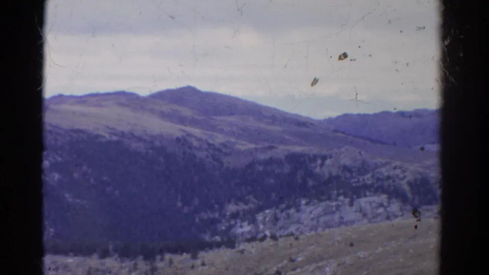 Colorado mountain landscape on 8mm film, showing layered ridges, tree-covered slopes, pale rocks, cloudy sky, and aged color shift.