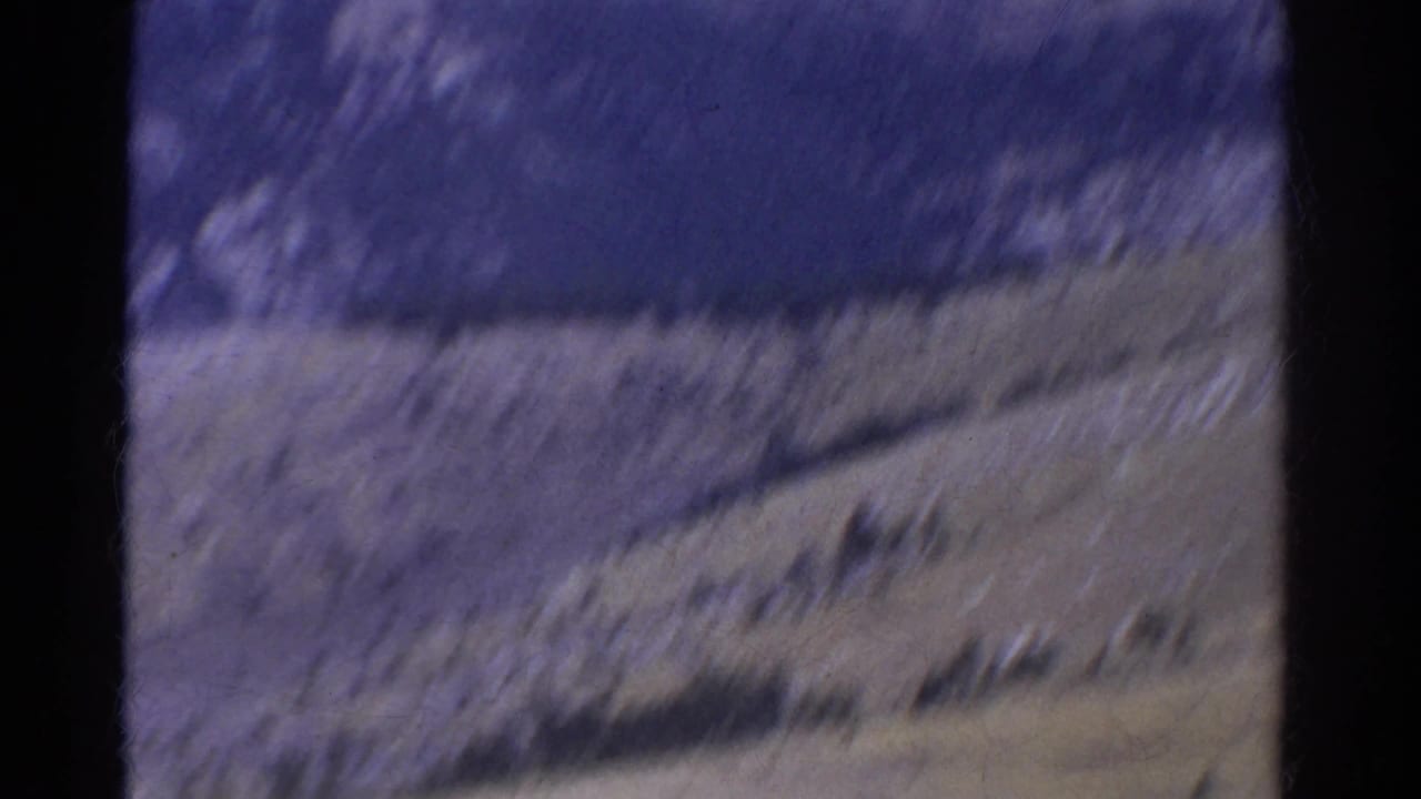 Blurred 1967 8mm Colorado mountain view with sloped terrain and dark frame edges during the start of a scenic pan.