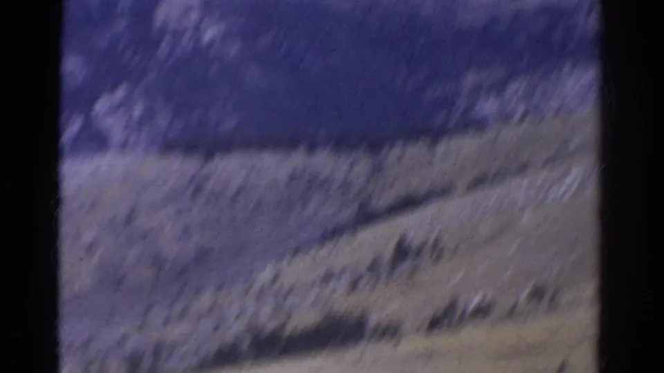 Blurred 1967 8mm Colorado mountain view with sloped terrain and dark frame edges during the start of a scenic pan.