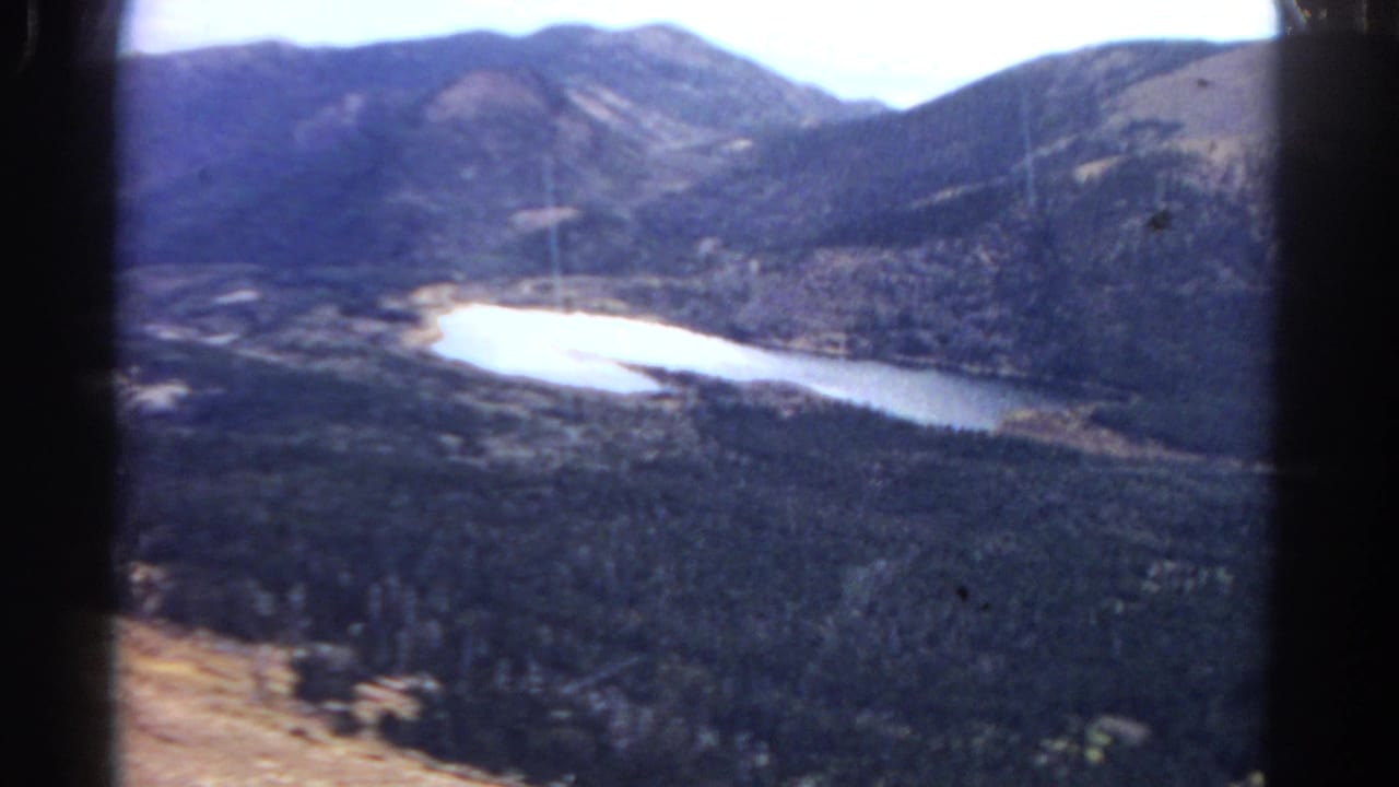 Forested mountain valley with a bright winding lake or river below rugged peaks.