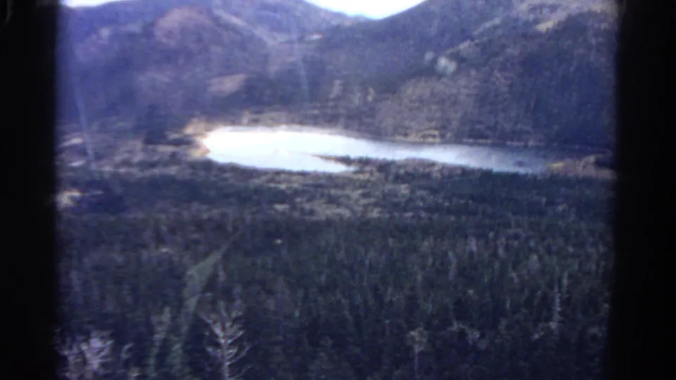 Final 1967 Colorado 8mm frame showing bright valley water, forested slopes, mountains, and heavy film borders.