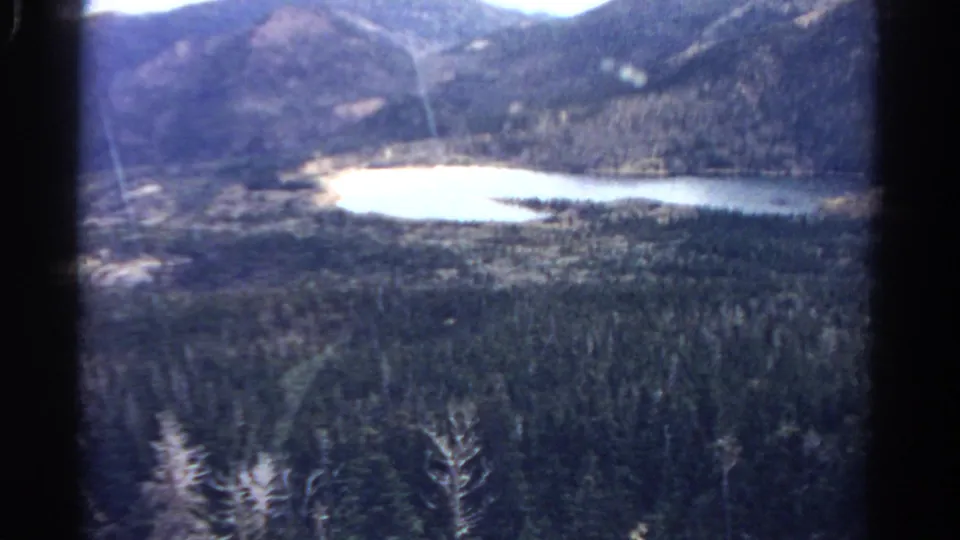 1967 Colorado 8mm still showing a soft, grainy view of lake water, dense trees, and surrounding hills.