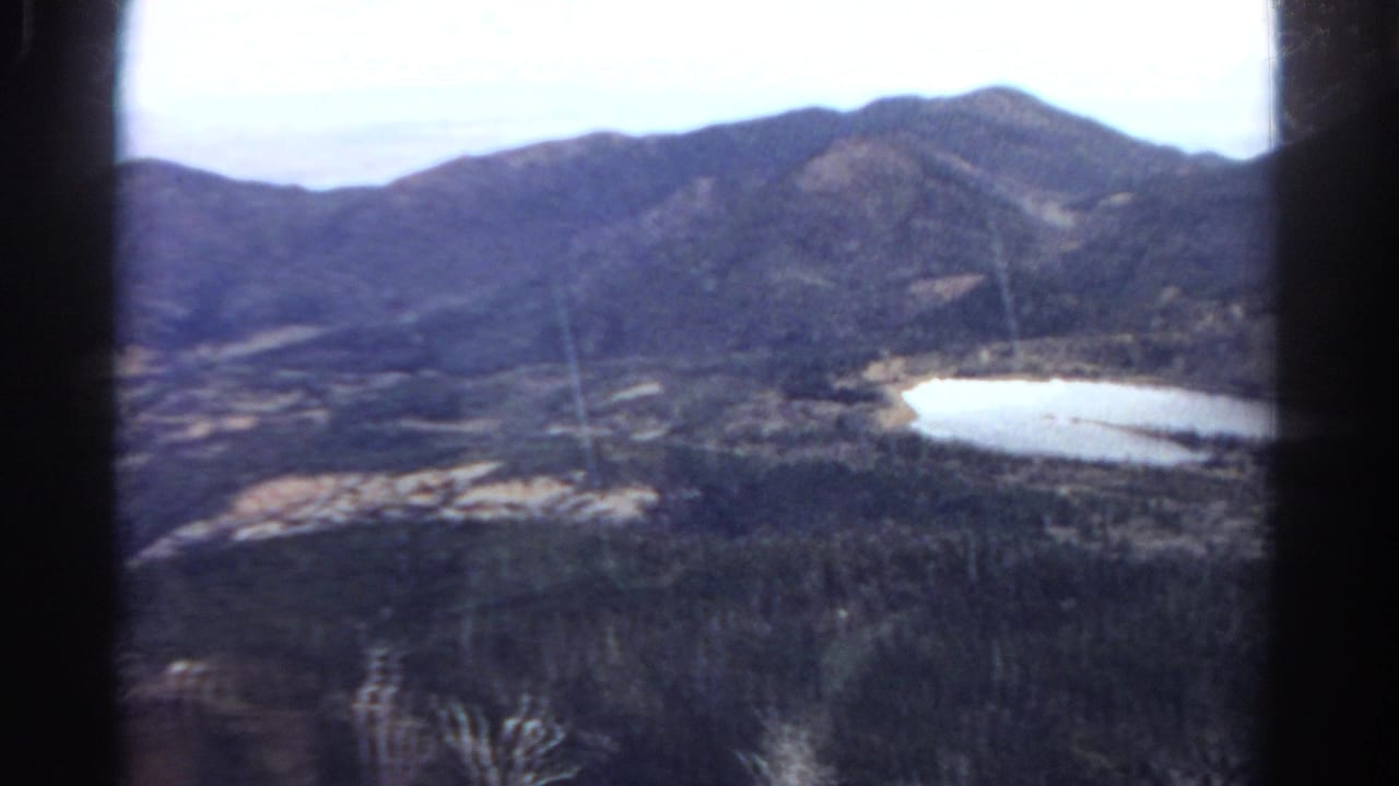 1967 Colorado home-movie view of mountains, forest, and a bright lake framed by dark window or film-strip edges.