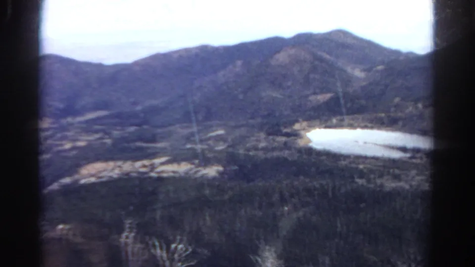 1967 Colorado home-movie view of mountains, forest, and a bright lake framed by dark window or film-strip edges.