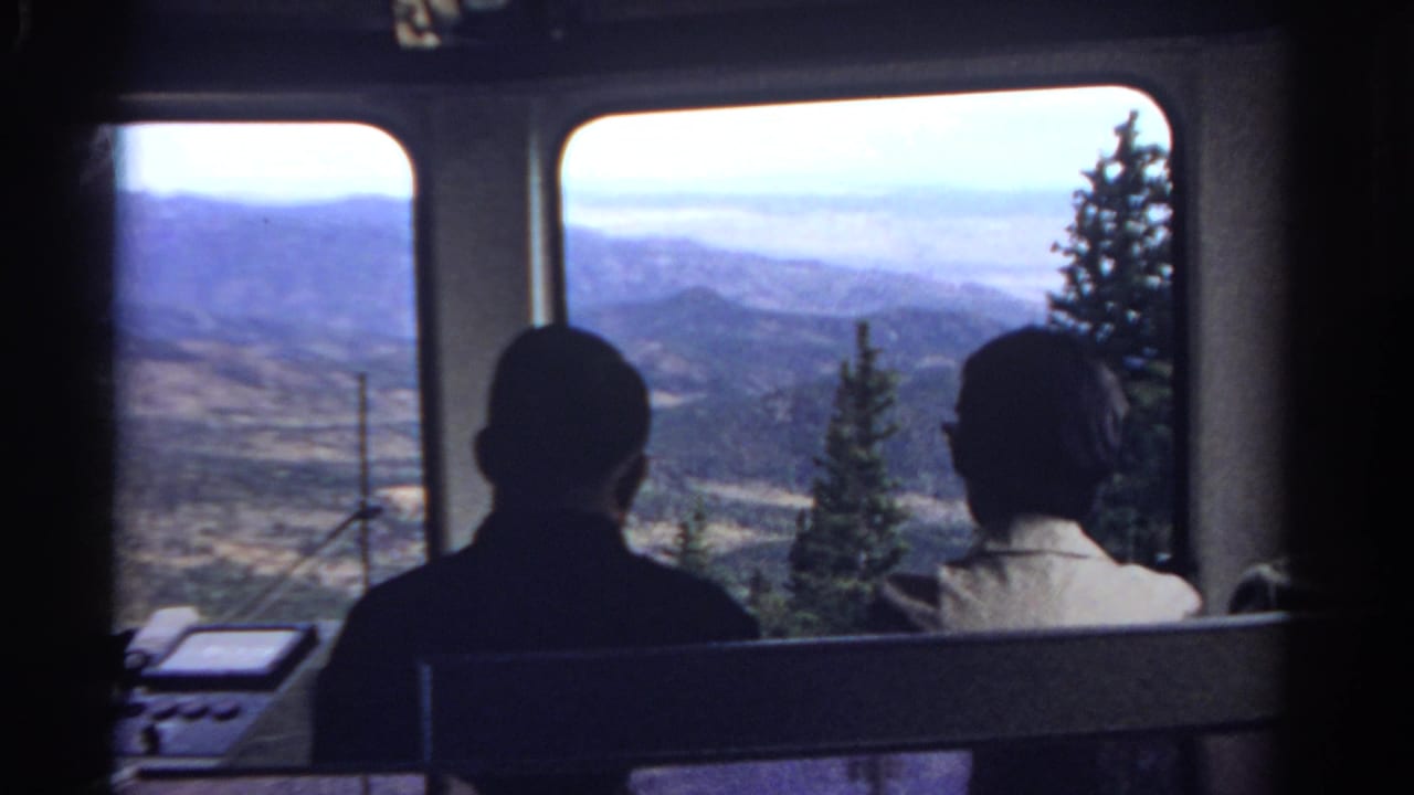 Silhouetted passengers look out tram windows toward a hazy mountain valley.