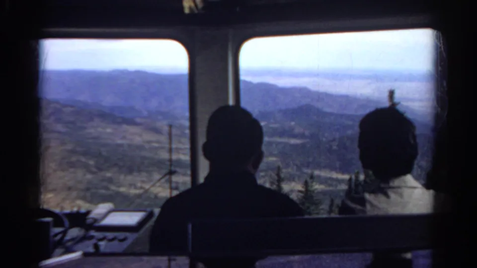 End frame of the 1967 Colorado tram ride, showing two silhouetted passengers and a sunlit mountain valley through the cabin windows.