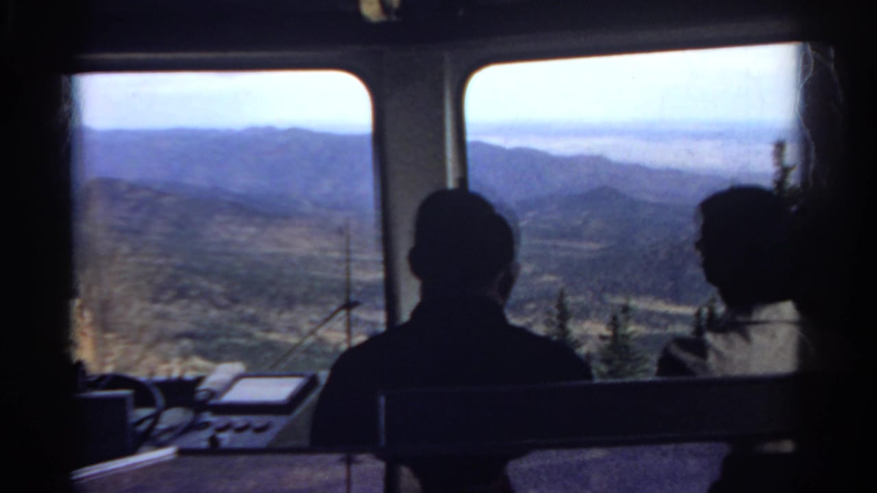 1967 Colorado 8mm frame of two passengers silhouetted inside a scenic vehicle, with mountains seen through large windows.