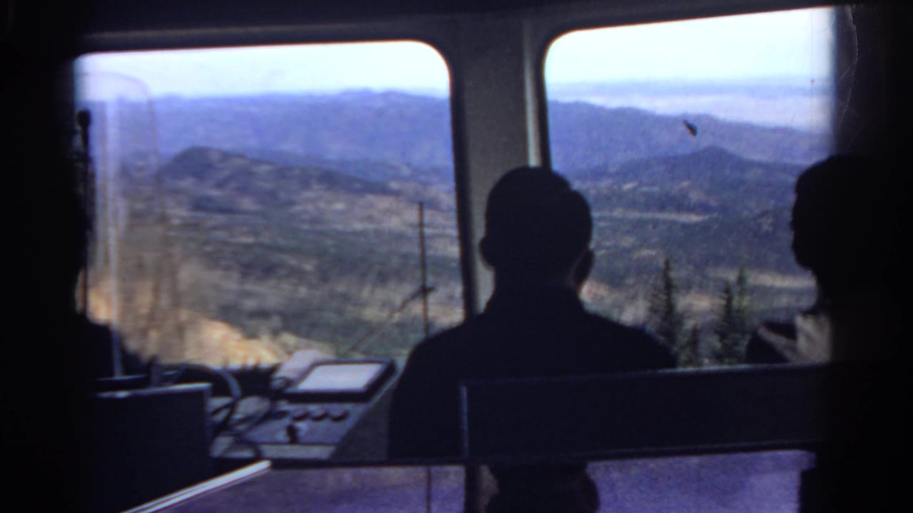 Silhouetted passengers in a Colorado scenic vehicle look out at distant mountain ridges and a valley through broad windows.