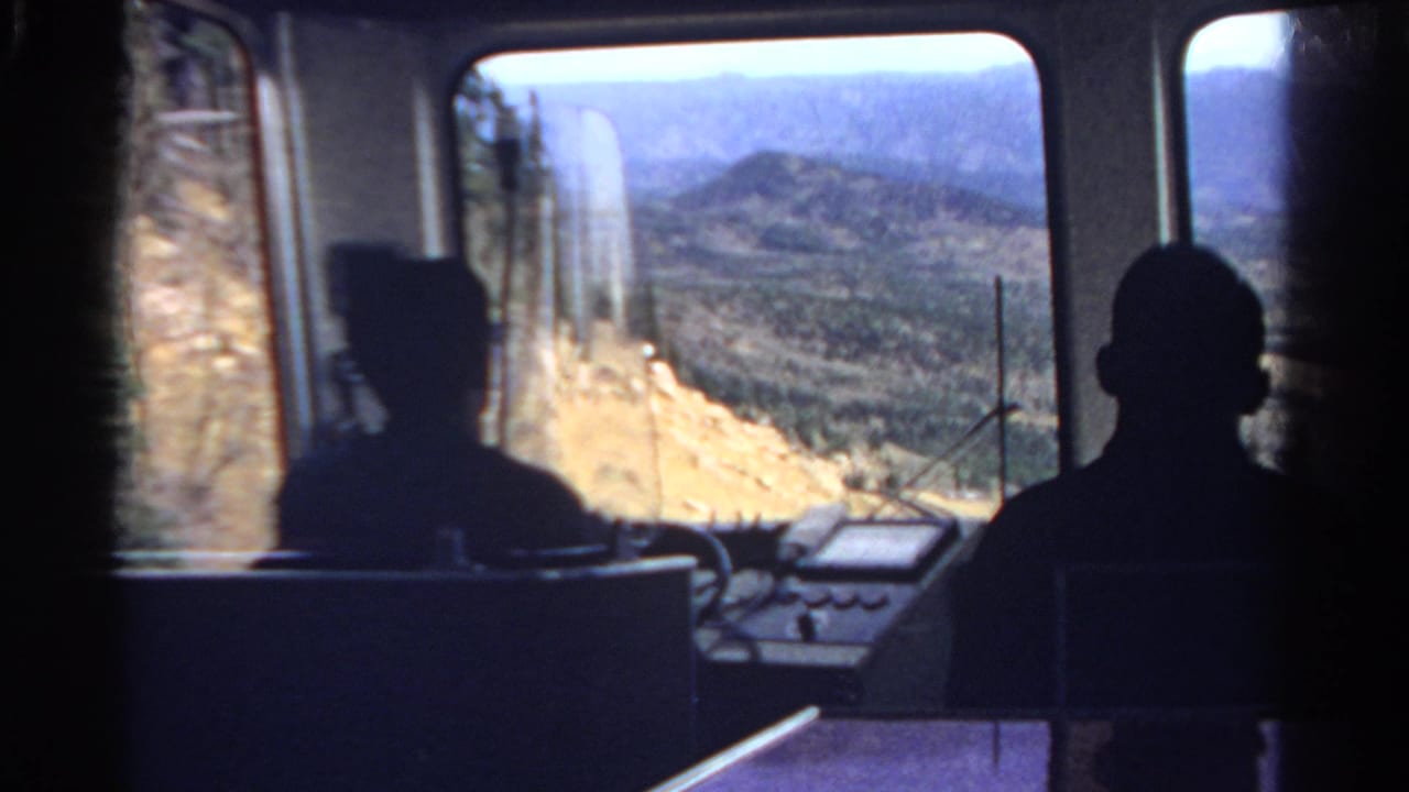 1967 Colorado 8mm frame showing silhouetted figures in a train cabin against bright mountain terrain outside.