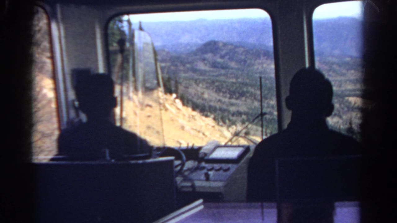 1967 Colorado train interior with dark seated figures and a bright view of hills, forest, and distant ridges.