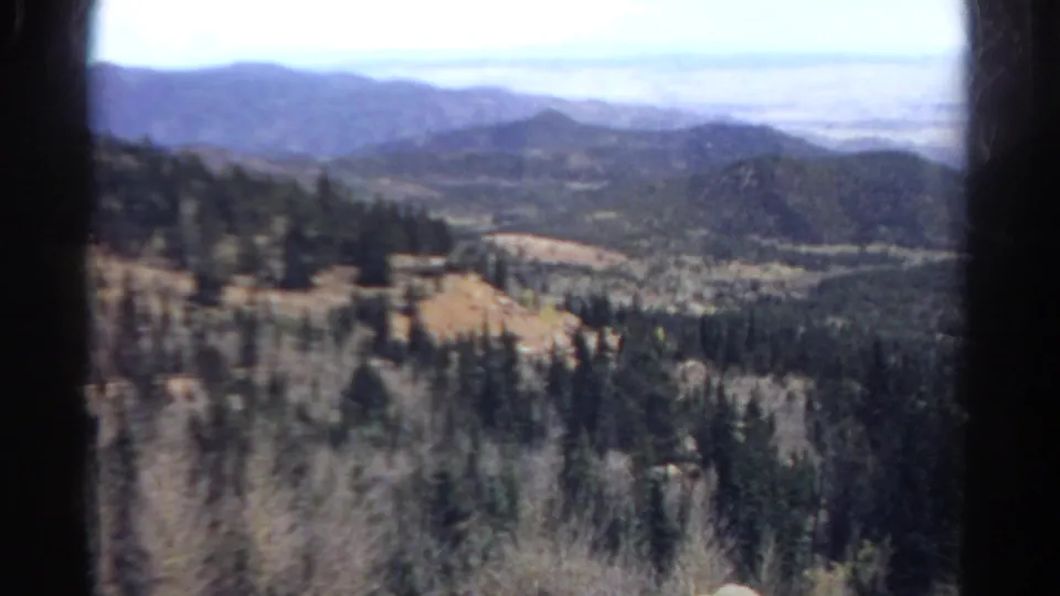 1967 Colorado 8mm view from a moving train across forested slopes, hills, and distant mountains.