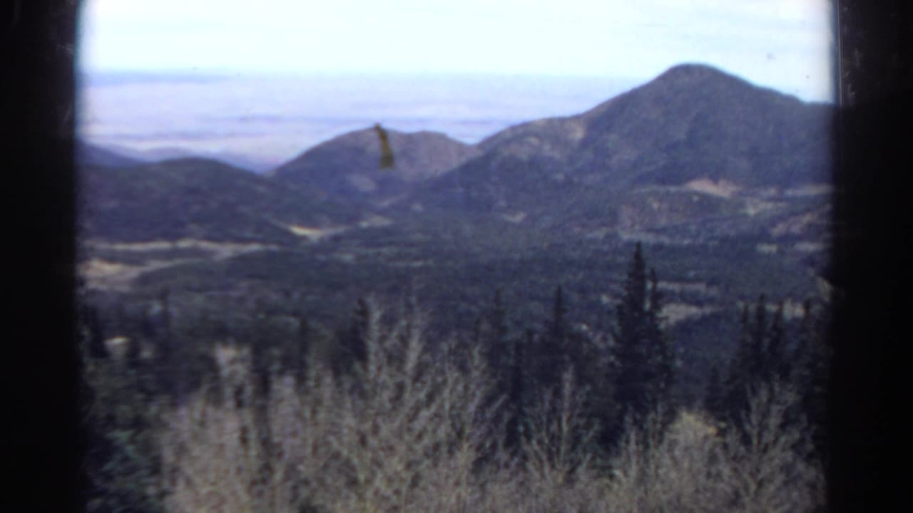 1967 8mm view of distant Colorado mountain peaks and forested hills framed by a vehicle window.
