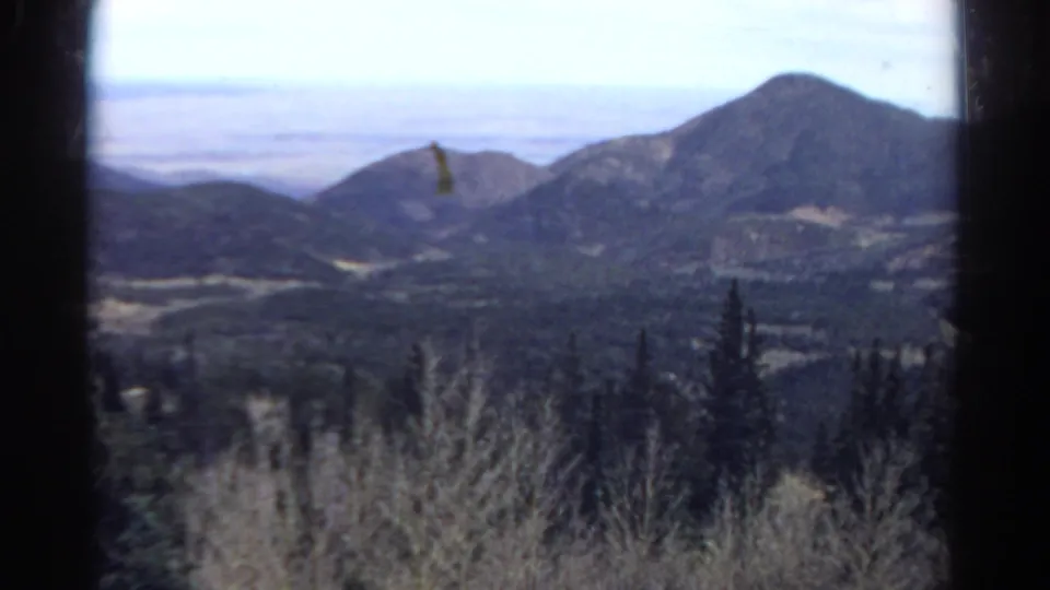 1967 8mm view of distant Colorado mountain peaks and forested hills framed by a vehicle window.
