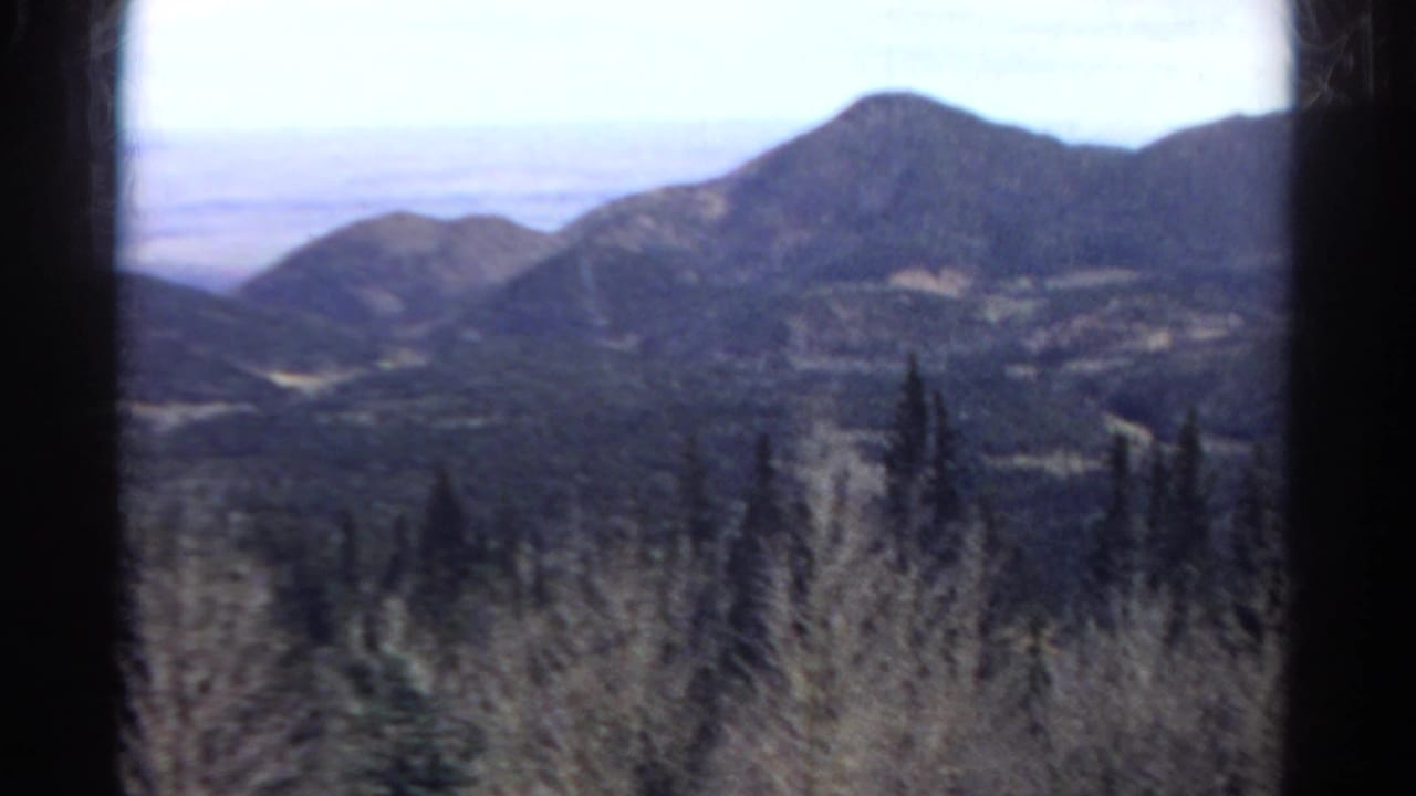 Colorado mountain scenery appears through dark window edges, with forested hills and distant peaks in soft 8mm focus.