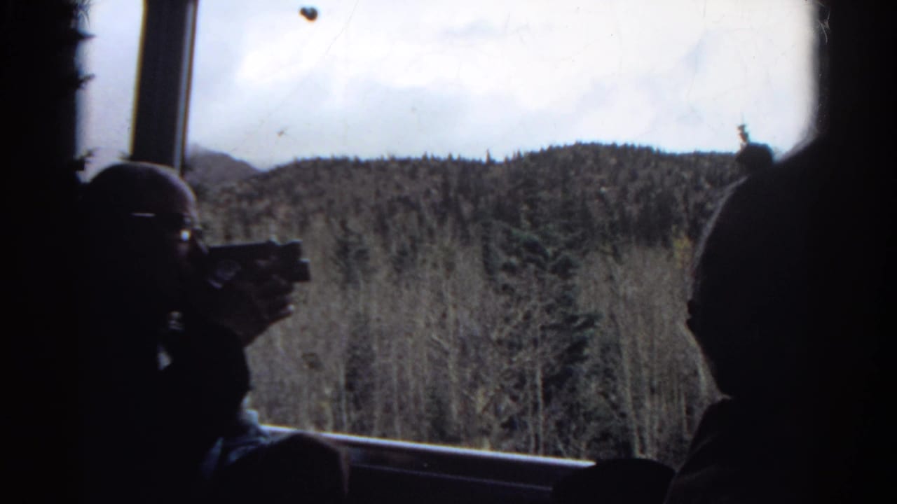 1967 Colorado 8mm frame showing a dark helicopter interior with a seated silhouette near the window and wooded mountain terrain outside.
