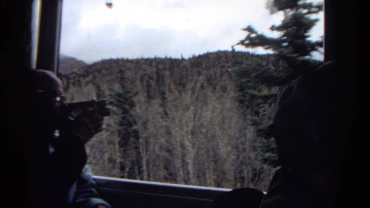 1967 Colorado 8mm frame with a central passenger silhouette and another dark figure at the edge, looking out over evergreen mountain forest.