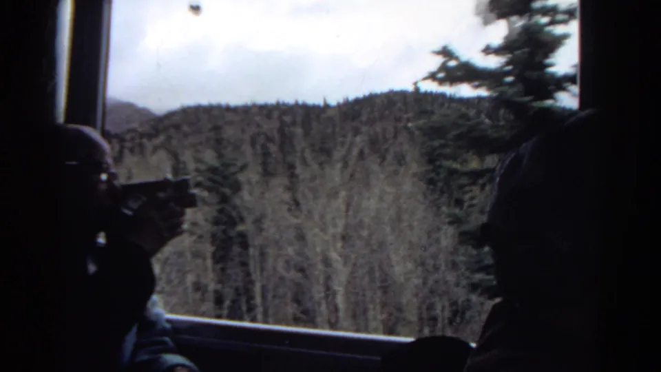 1967 Colorado 8mm frame with a central passenger silhouette and another dark figure at the edge, looking out over evergreen mountain forest.