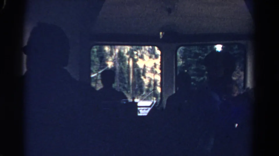 Silhouetted passengers sit inside a moving Colorado train in 1967, with sunlit trees and mountain scenery visible through the carriage windows.