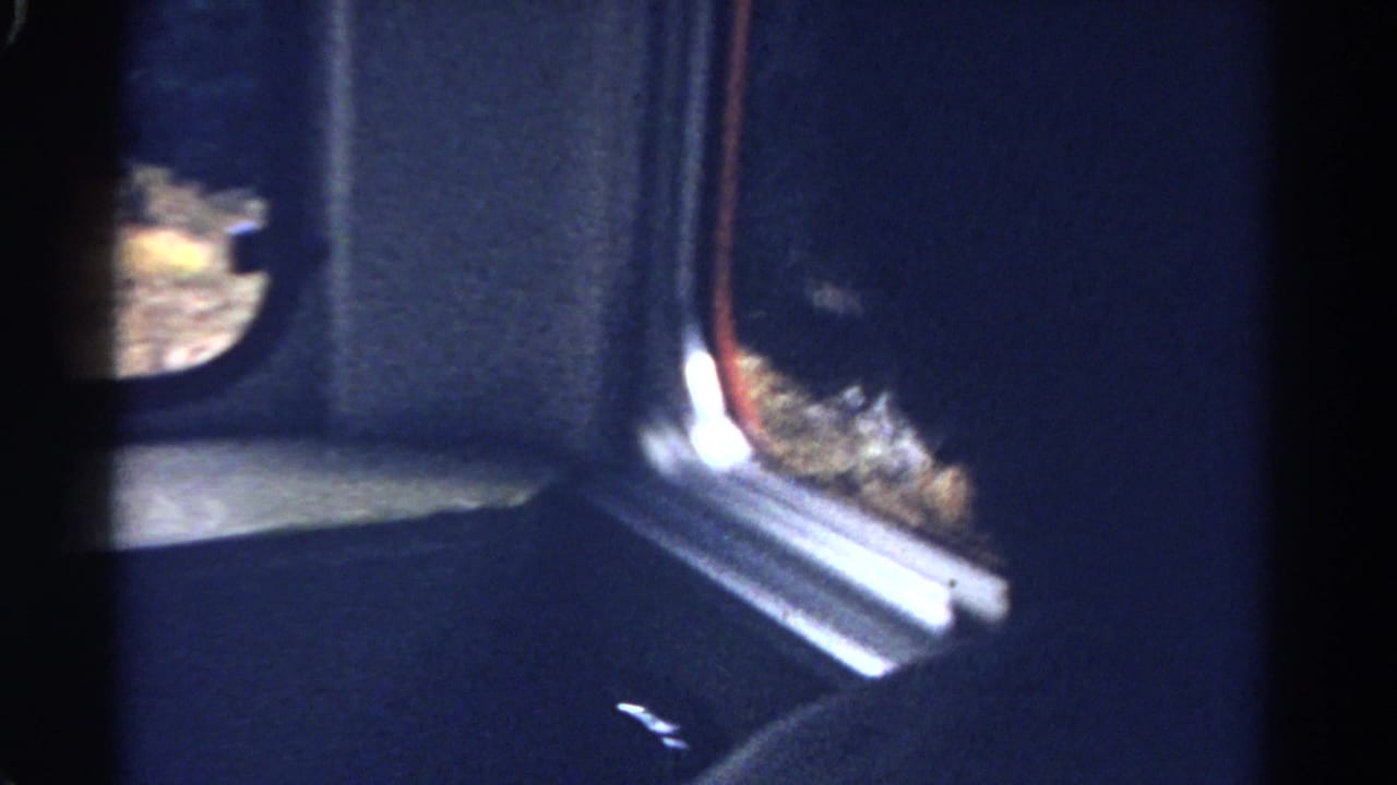 Interior passenger-window view from 1967 Colorado train footage, with dark framing, bright outdoor glimpses, and soft 8mm exposure.