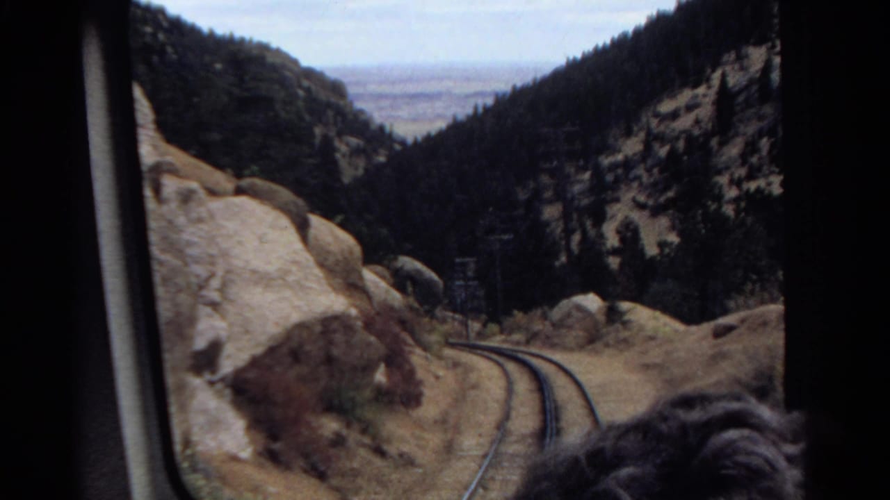 1967 Colorado 8mm view from a train window as tracks bend between boulders and pine-covered slopes.