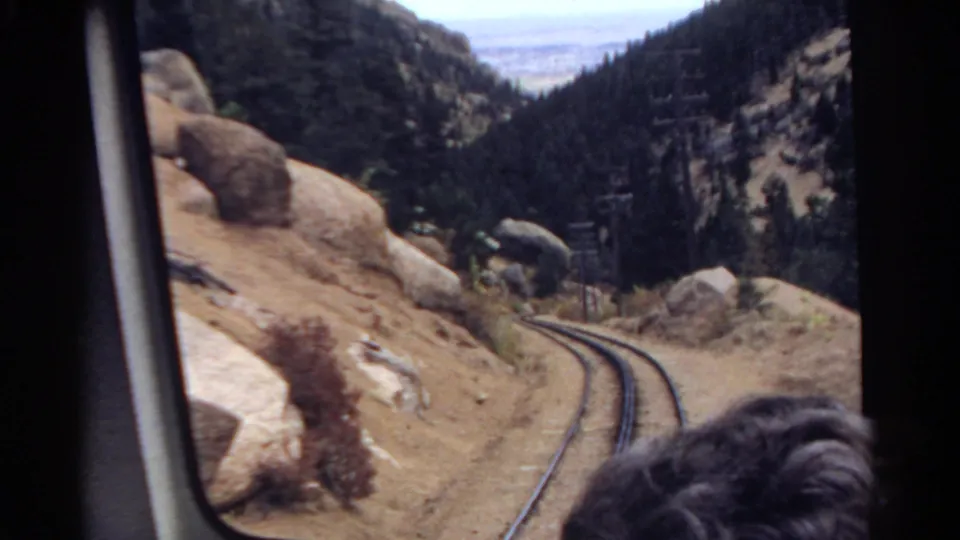 Colorado 1967 8mm frame of a rail curve through boulders and pine-covered mountains, filmed from inside a moving train.