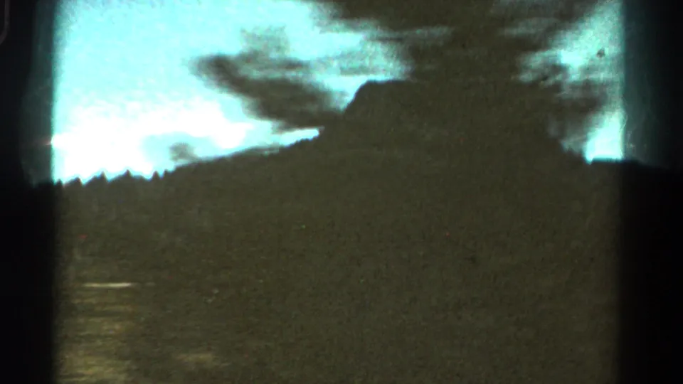 1967 Colorado home-movie frame with a silhouetted mountain ridge, treeline, and pale sky from a roadside view.