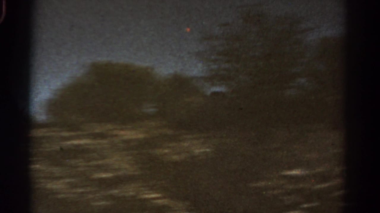 1967 Colorado 8mm frame with a dark mountain silhouette, roadside blur, trees, and twilight sky.