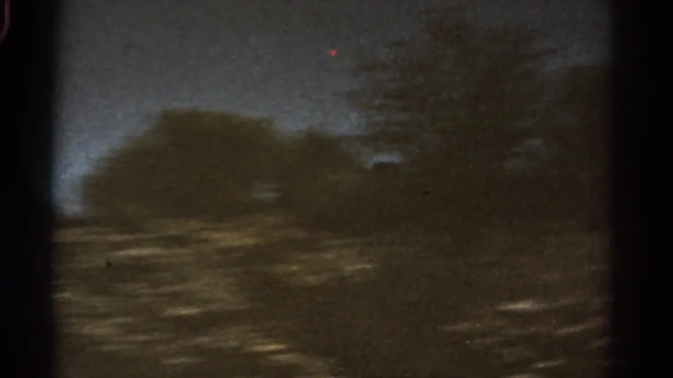 1967 Colorado 8mm frame with a dark mountain silhouette, roadside blur, trees, and twilight sky.