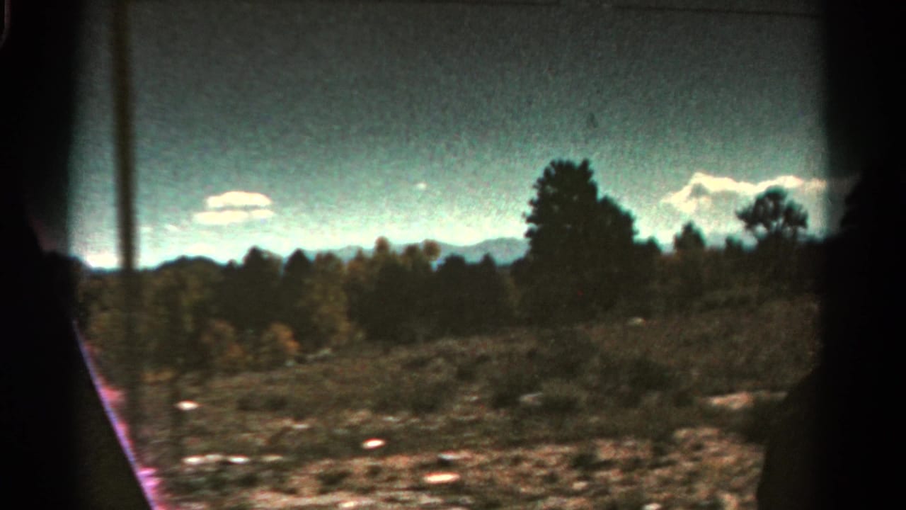 Moving view of scrubby terrain, scattered trees, distant mountains, and clouds with dark film borders.