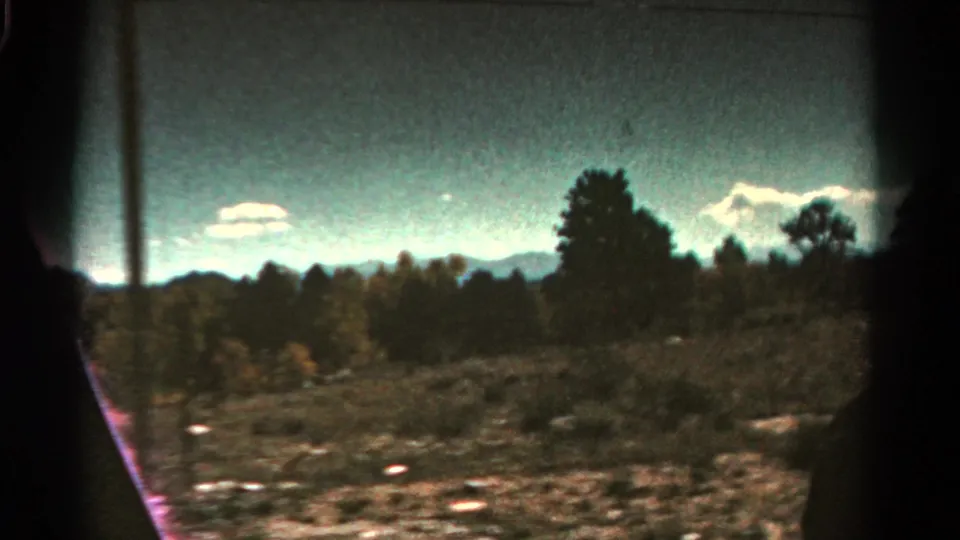 1967 Colorado 8mm frame showing open scrubland, tree silhouettes, distant mountain ridges, pale clouds, and visible film gate edges.