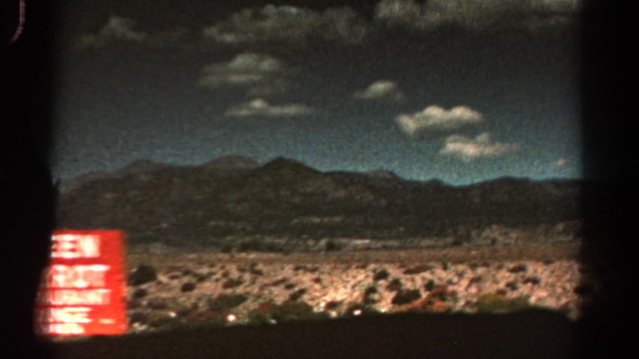Distant mountains and dry scrubland seen past a red roadside restaurant-lounge sign.