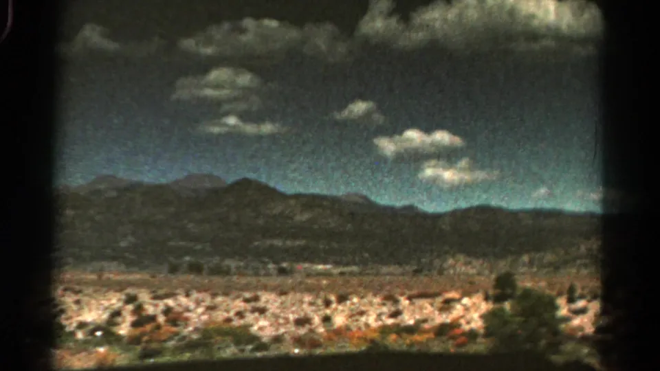 1967 Colorado home-movie frame with distant mountains, dry scrubland, textured clouds, and pronounced 8mm frame borders.