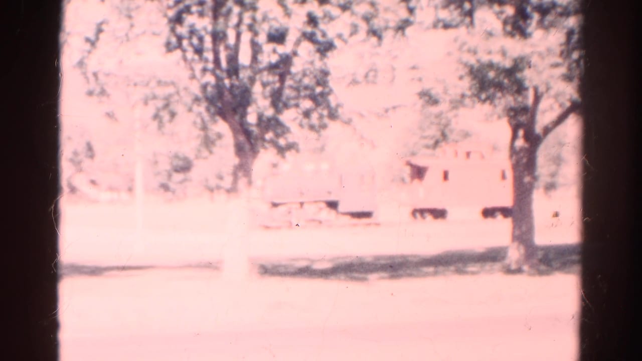 1967 Colorado home-movie frame showing a faint outdoor scene with trees and a small train-car-like object behind heavy overexposure.