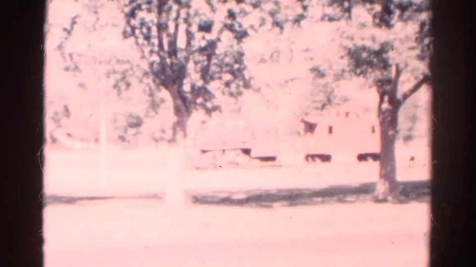 1967 Colorado home-movie frame showing a faint outdoor scene with trees and a small train-car-like object behind heavy overexposure.