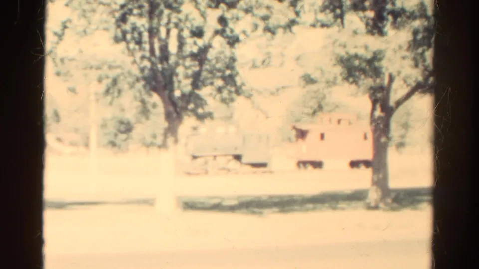 Final 1967 Colorado frame with yellow-pink film color, tree canopy, dark trunk, pale ground, and a small rail-car-like background form.