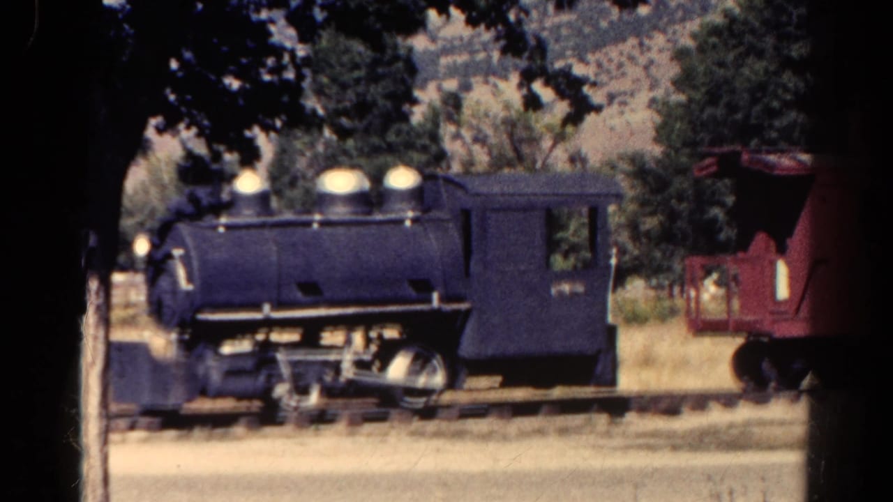 1967 Colorado home-movie frame with a dark blue steam-style locomotive on rails and a red caboose partly visible to the right.