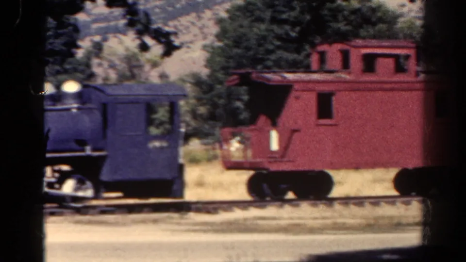 1967 Colorado 8mm frame showing the red caboose more clearly behind the blue locomotive, with trees framing the parked train.