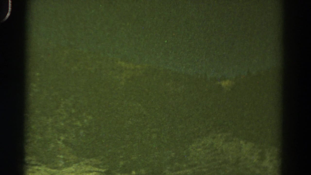 Low-light 1967 Colorado 8mm view of a snowy or frosted mountain slope, tinted green and partly framed by dark film edges.