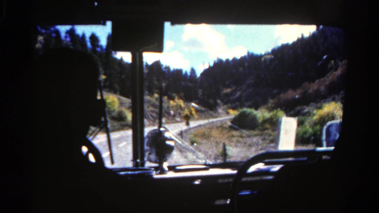 1967 Colorado 8mm frame showing a dark driver silhouette and dashboard against a bright winding road through dry hills.