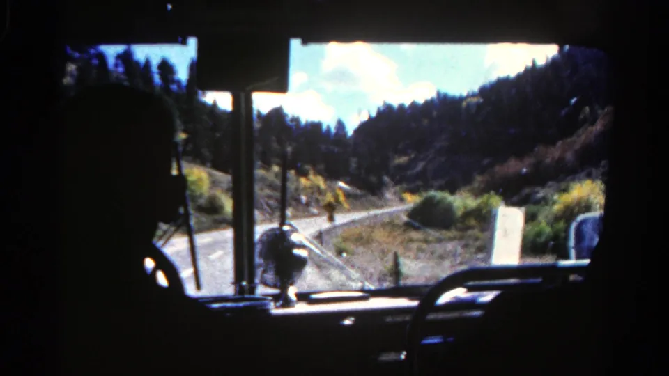1967 Colorado 8mm frame showing a dark driver silhouette and dashboard against a bright winding road through dry hills.