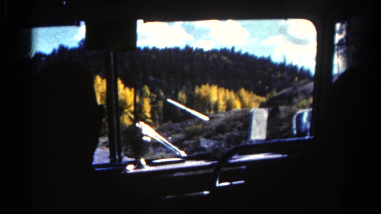 Interior car-window view in 1967 Colorado, with silhouetted seats and wooded hills visible outside.
