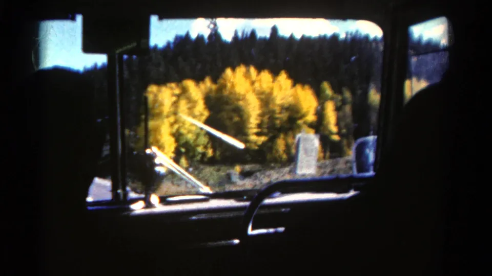 Final 1967 Colorado frame from inside the car, with passengers in silhouette and autumn forest passing outside.