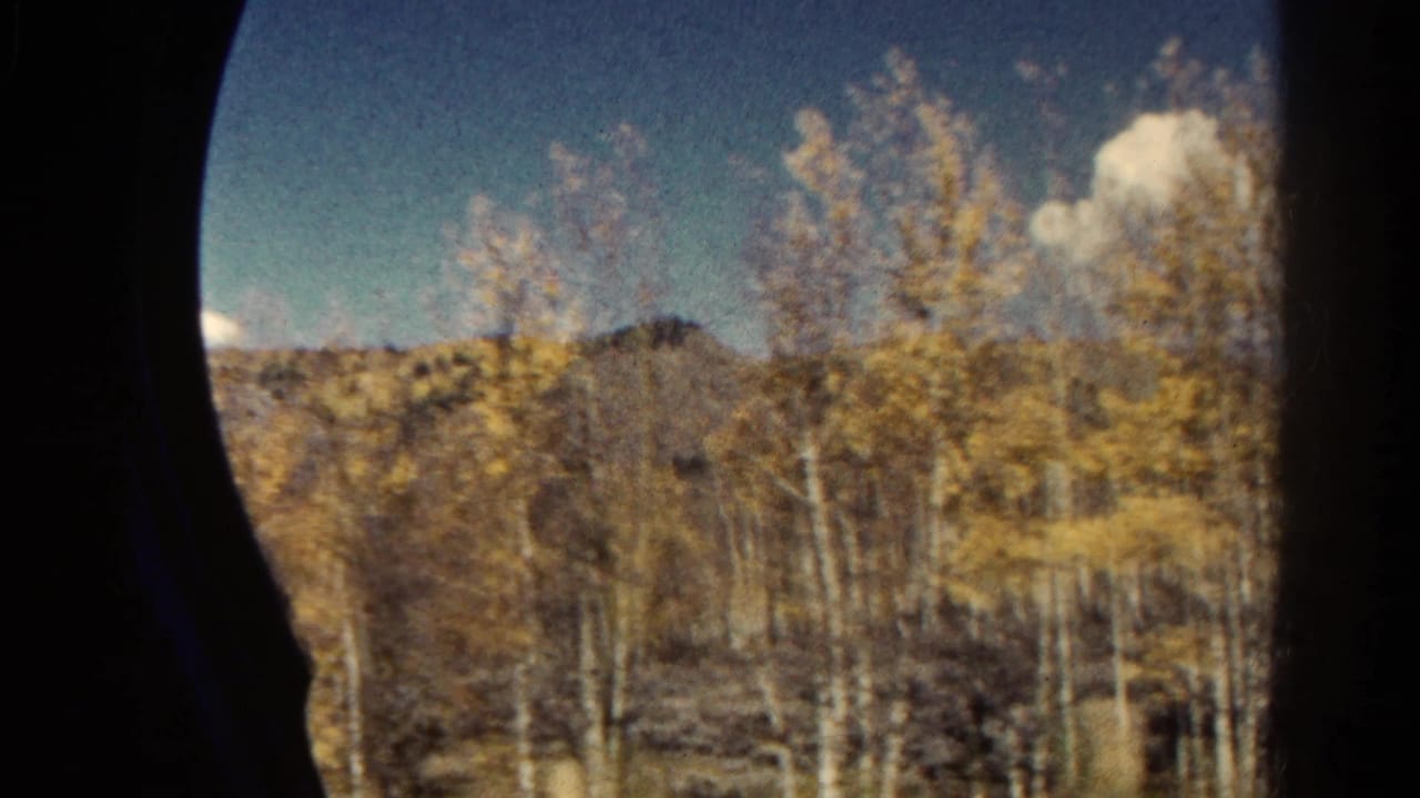 Colorado mountain countryside seen from a moving train, with yellow aspen foliage, distant ridge, blue sky, and dark window framing.