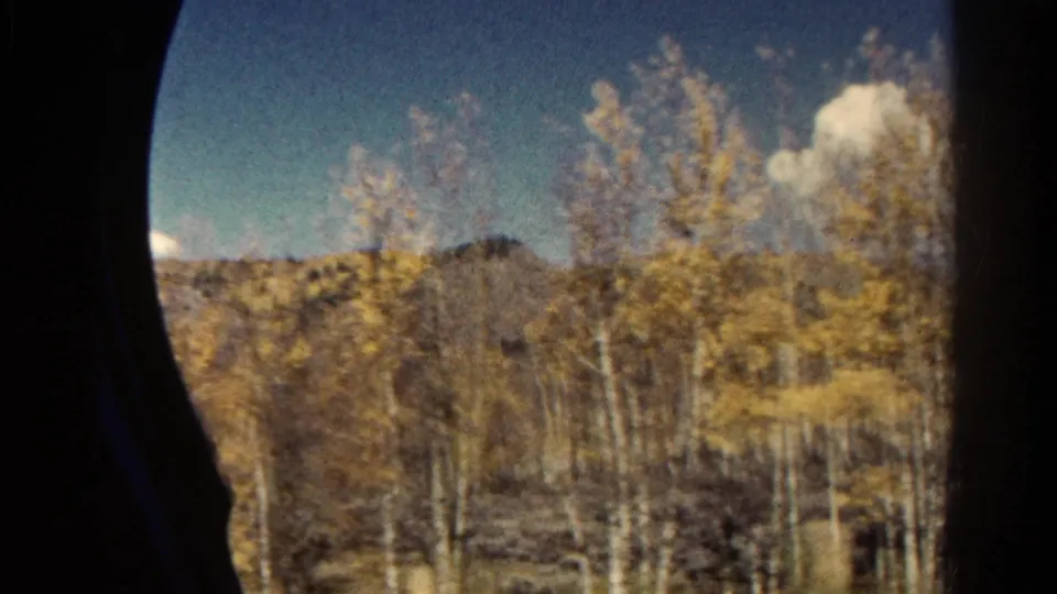 Colorado mountain countryside seen from a moving train, with yellow aspen foliage, distant ridge, blue sky, and dark window framing.