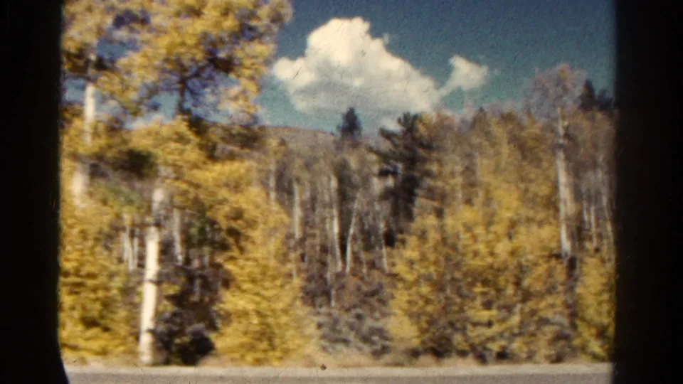 1967 Colorado travel frame with roadside aspens, distant hills, white clouds, and motion-softened 8mm color texture.