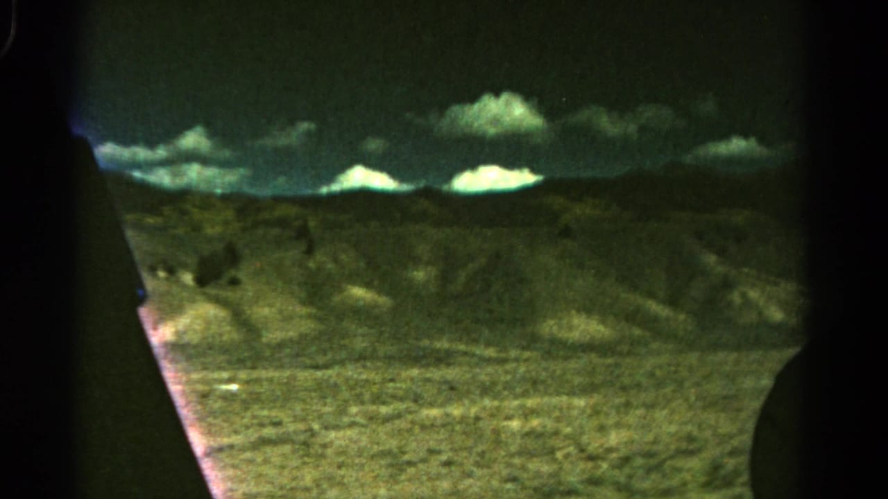 Rolling hills beneath bright clouds, partly framed by dark vehicle-window edges.
