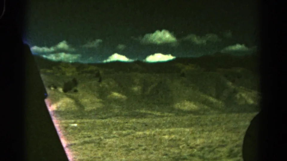 1967 Colorado 8mm frame showing open hills and clouded sky seen through dark vehicle-window edges.