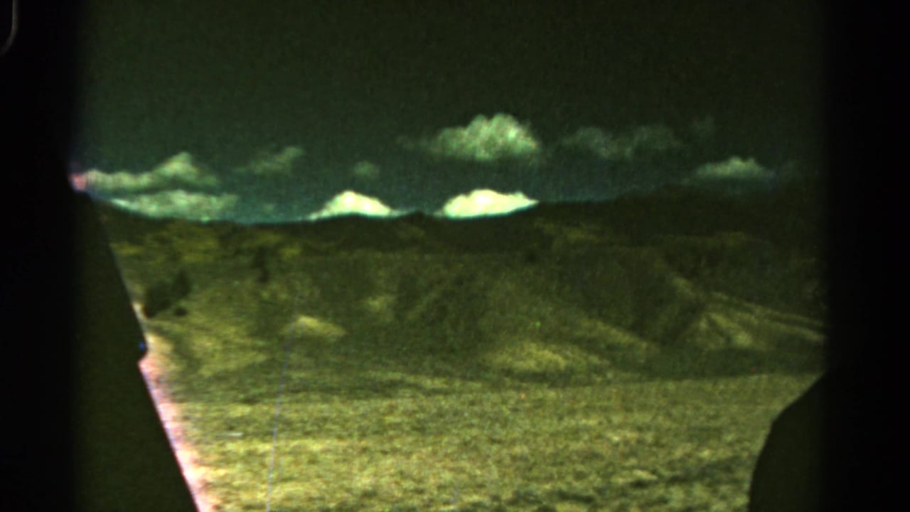 1967 Colorado travel footage frame with muted hills, pale clouds, and a dark vehicle or film edge at center.