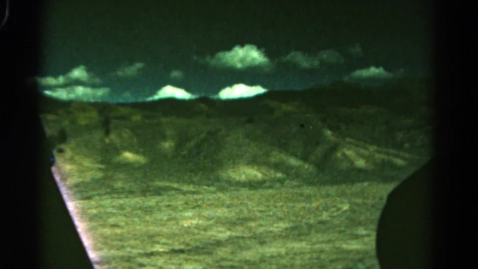 1967 Colorado 8mm frame with rough hillside terrain, bright clouds, and visible window or gate edges.