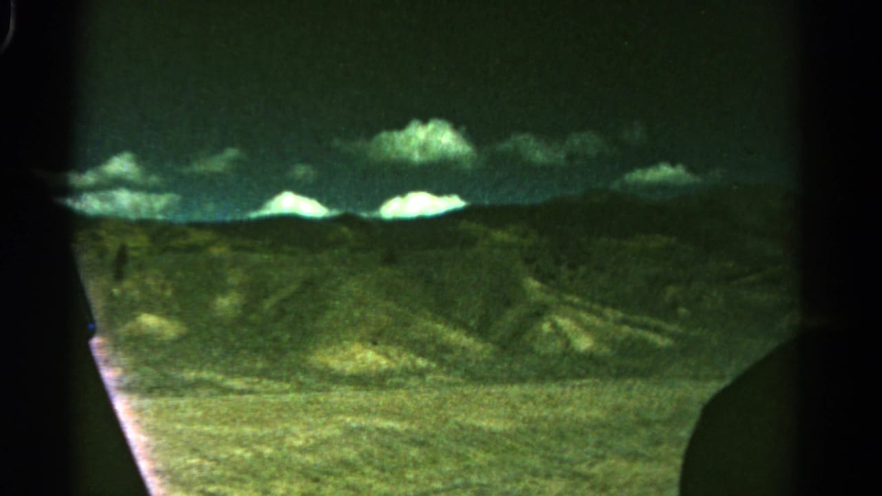 Rolling hills and distant mountains under clouds, seen through dark frame edges.